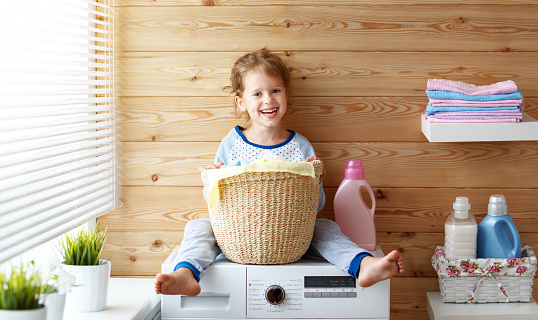 happy little funny housewife baby girl in laundry   with washing machine