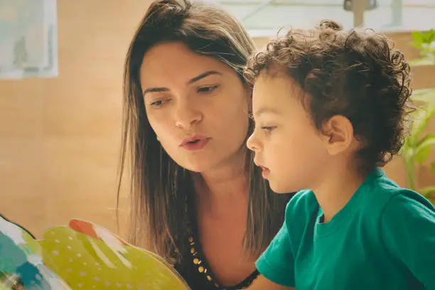 Mother teaching her two years old son with a children's book.