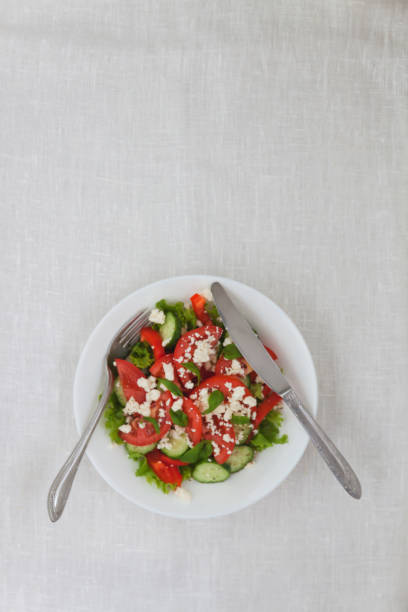 Shopska salad in a white plate on a white tablecloth. The concept of minimalism stock photo