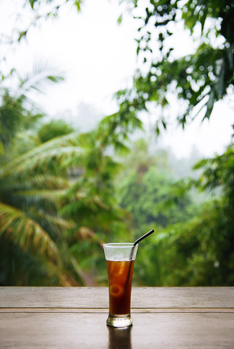 Wood table with iced coffee behind blurred tropiccal rain forest.Ubud Bali Indonesia