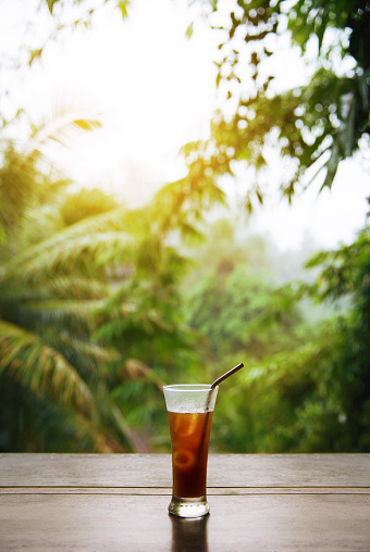 Wood table with iced coffee behind blurred tropiccal rain forest.Ubud Bali Indonesia