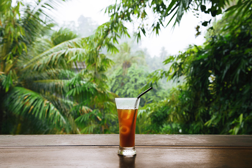 Wood table with iced coffee behind blurred tropiccal rain forest.Ubud Bali Indonesia