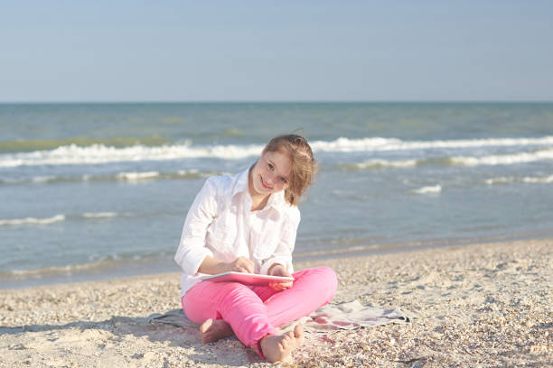 La diciassettenne con sindrome di Down in spiaggia gioca con il tablet. - foto stock