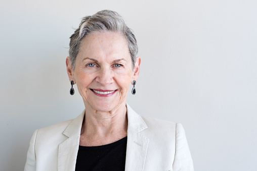 Head and shoulders view of beautiful older woman with short grey hair and beige jacket against neutral background (selective focus)