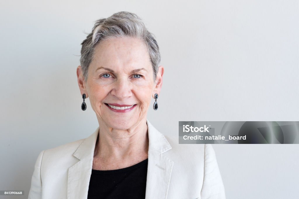 Older woman in beige jacket Head and shoulders view of beautiful older woman with short grey hair and beige jacket against neutral background (selective focus) Senior Women Stock Photo