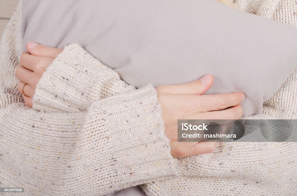 Gros plan des mains de la jeune fille dans un chandail de laine beige occasionnels étreignant un oreiller gris - Photo de Se mettre les bras autour du corps libre de droits