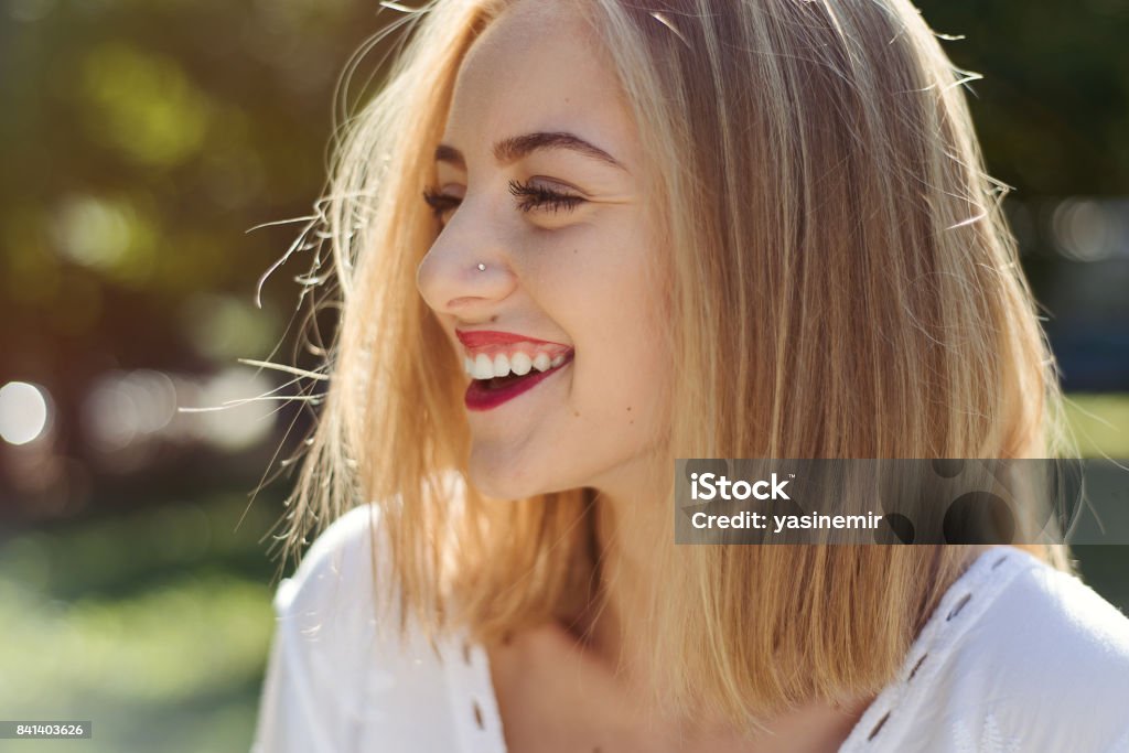 Headshot photo of a young pretty girl smiling in nature Headshot photo of a young pretty girl in nature smiling and looking away in a sunny day, close-up portrait of a female fashion blogger giving happy face expression in nature. Young cute girl looking away and laughing, Summer Stock Photo