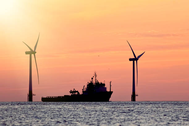 istock Sustainable resources. Wind farm with ship silhouette at tropical sunrise or sunset. Solar and wind energy and food supply represented. 841404776