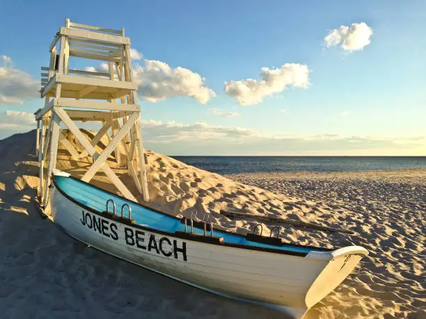 A lifeboat and lifeguard chair on the sand with the Atlantic ocean in the background at Jones Beach State Park in Wantagh, Long Island, NY.