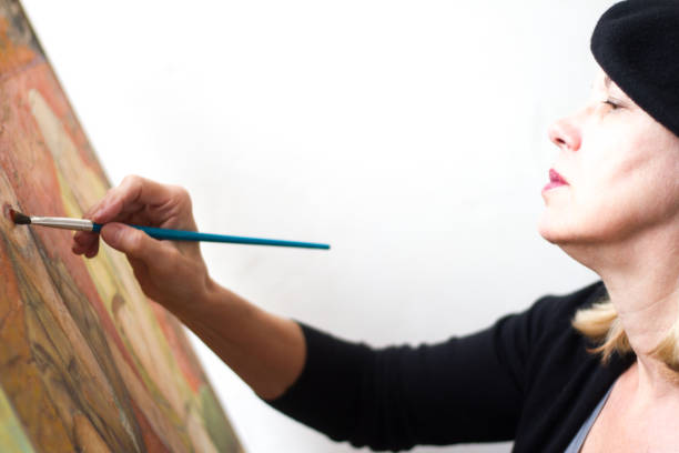 Female Artist with Beret Painting (Close-Up) Female senior artist with black beret paints an oil portrait (close-up); white background with copy space painted image paintings oil paint senior women stock pictures, royalty-free photos & images