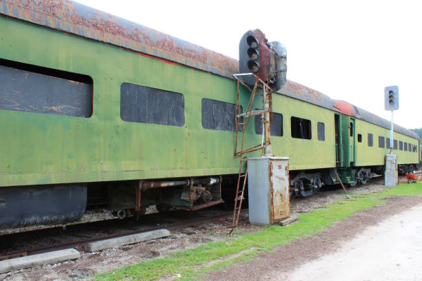 istock Green abandoned passenger train cars with boarded windows beside light posts on train tracks 841419546