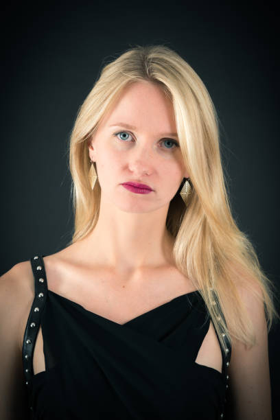 Blonde woman in urban background. Beautiful young girl wearing black elegant dress standing in the street. Pretty russian female with long wavy hair hairstyle and blue eyes.