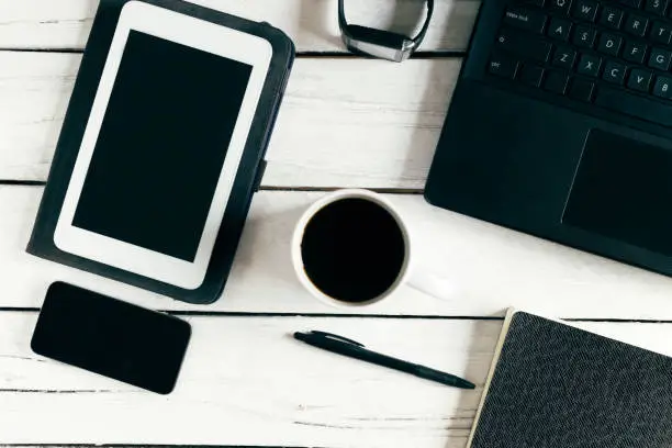 Modern working space with a laptop, a cup of coffee, a pen, a smartphone, a notebook, a tablet, a smart watch. View from above. On a white wooden background