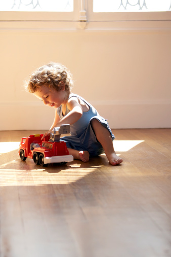 side view of a baby boy playing with car toy on white background