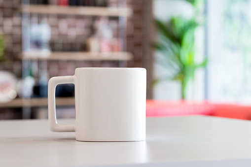 White mug in morning time at office room background. Blank drink cup for your design. Square shape.