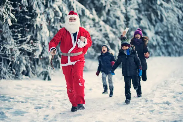 Santa Claus spotted in the forest by a group of children. Santa is running away from the children that are chasing after him.
