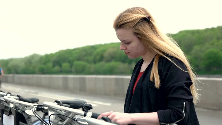 Girl rents a bicycle in parking lot. Woman pays a bicycle rent with plastic card