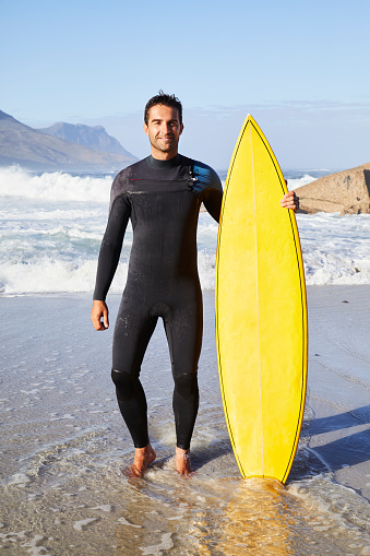 Surfer dude in wetsuit standing with board on beach