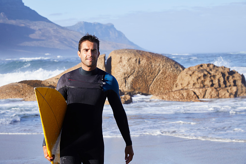 Surfer dude in wetsuit carrying board on beach