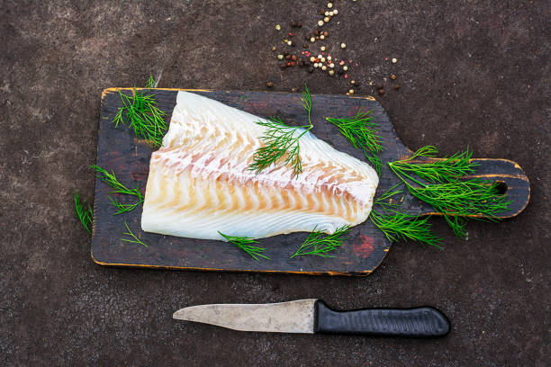 istock Raw cod before cooking on a black chopping Board with herbs and sea salt on a dark background. Top view 841490414