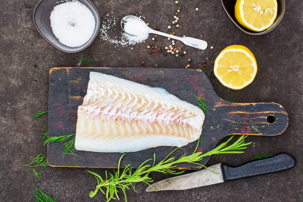 istock Raw cod before cooking on a black chopping Board with herbs and sea salt on a dark background. Top view 841490416