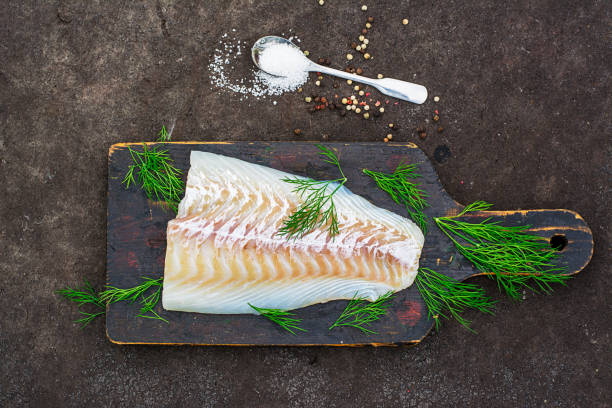istock Raw cod before cooking on a black chopping Board with herbs and sea salt on a dark background. Top view 841490420