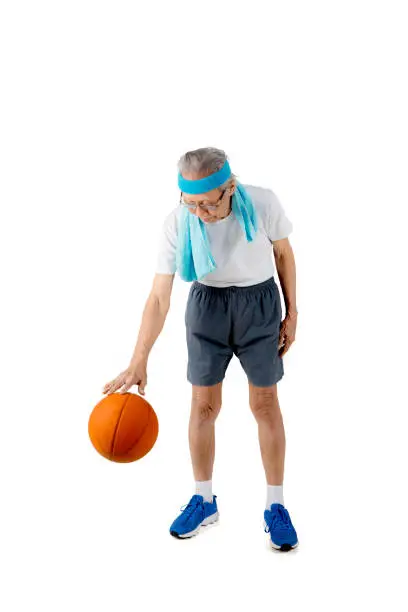 Portrait of an elderly man is dribbling a basketball in the studio, isolated on white background