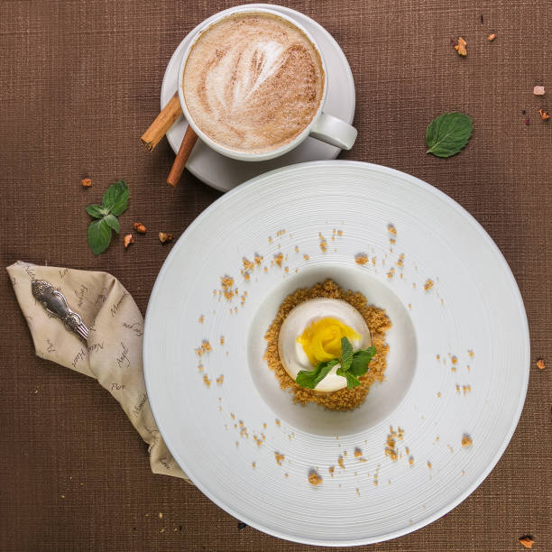 istock Mango cake, mousse dessert on a white plate with cup of coffee cappuccino on the brown table. Top view. 841491424