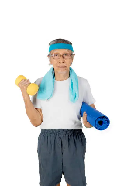 Portrait of an elderly man looking at the camera while holding a barbell and mat, isolated on white background