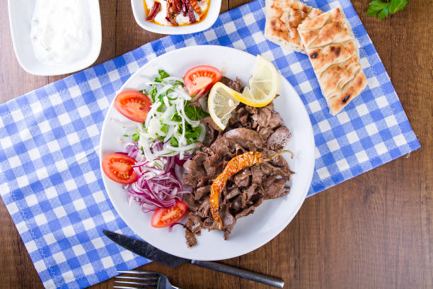 Turkish and Arabic Traditional Liver Doner Kebab serving witt salad, yogurt, lettuce, pita bread, onion, tomato and rice pilav in white plate on garnish restaurant background stock photo