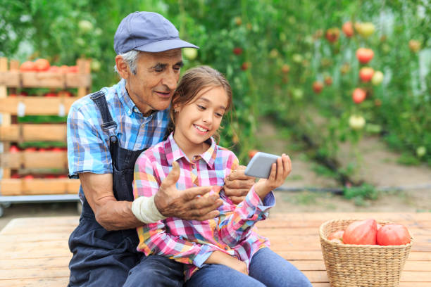 little girl and mature farmer using smart phone in the garden - casual granddaughter farmer expressing positivity imagens e fotografias de stock