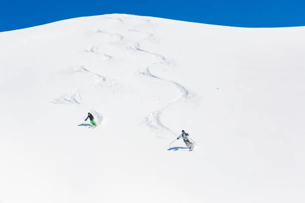 Man and woman skiing down mountain leaving tracks behind