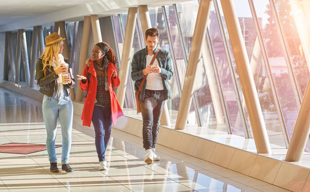 3 young adults entrepreneurs or students group mixed race walking with coffee and cellphone stock photo