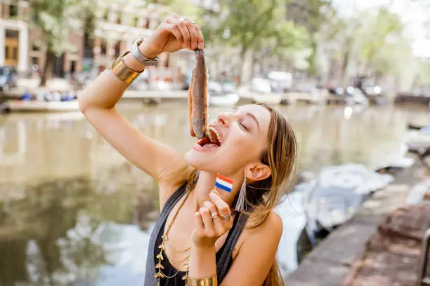 Young woman eating fresh harring standing outdoors in Amsterdam city. Harring with onion is a traditional dutch snack