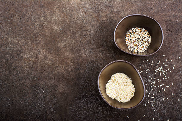 Sesame black, brown and white in dark ceramic bowls on a dark background. Top View