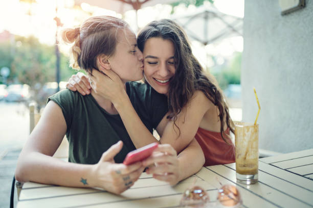 Sharing some love Young happy women drinking ice coffee outdoors on a hot summer day, embracing, kissing and having fun gay long hair stock pictures, royalty-free photos & images