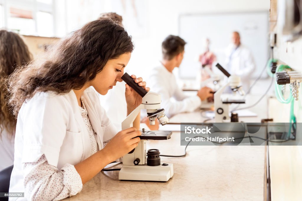 Estudante do colegial linda com microscópio no laboratório. - Foto de stock de Ciência royalty-free