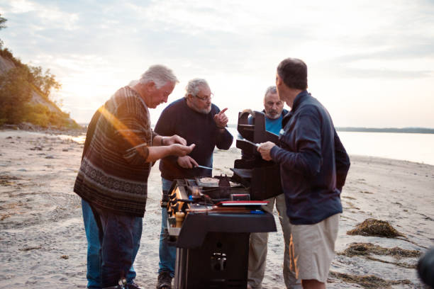 Social Seniors brothers barbecue activity Five Social Seniors brothers making barbecue activity on a beach at the evening. They are cooking fish and tasting it. The fisherman have fun. The photo was taken in Quebec Canada. It is horizontal and color image. family bbq beach stock pictures, royalty-free photos & images