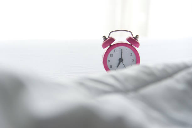 istock Pink Alarm clock on bed in morning with sun light 841567256