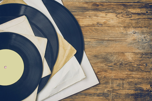 pile of old vinyl records in paper cover lie on wooden table, retro style, top view