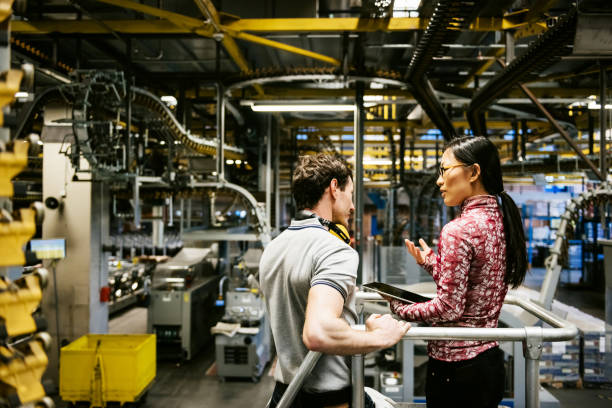 Mechanic And Female Engineer Talking in Factory Mechanic and manager talking nearby a machine in a big printery about latest newspaper print industrial equipment stock pictures, royalty-free photos & images