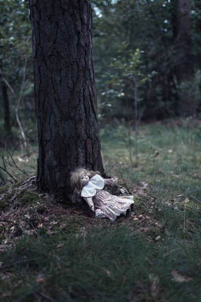 istock Spooky doll girl on forest ground against tree trunk. 841595710