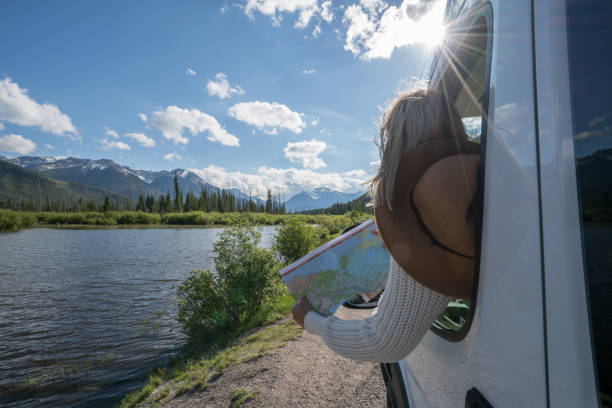 Young woman looks at road map near mountain lake Young woman in car on mountain road looks at map for directions. Mountain lake landscape in Springtime with snow melting. canada road map stock pictures, royalty-free photos & images