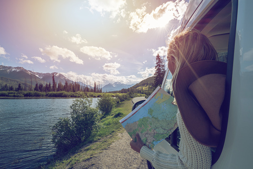 Young woman in car on mountain road looks at map for directions. Mountain lake landscape in Springtime with snow melting.