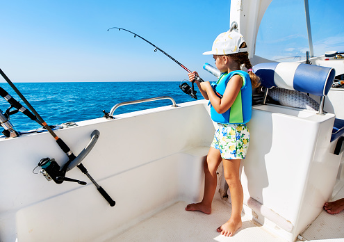Lovely little girl with a fishing rod fishing on the boat