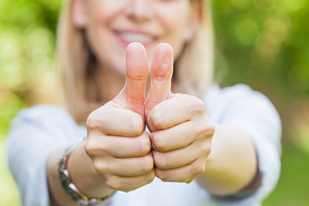 Close up picture of smiling woman showing thumbs up outdoor