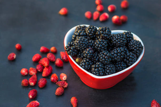 fresh blackberries in bowl shape heart on black stone background
