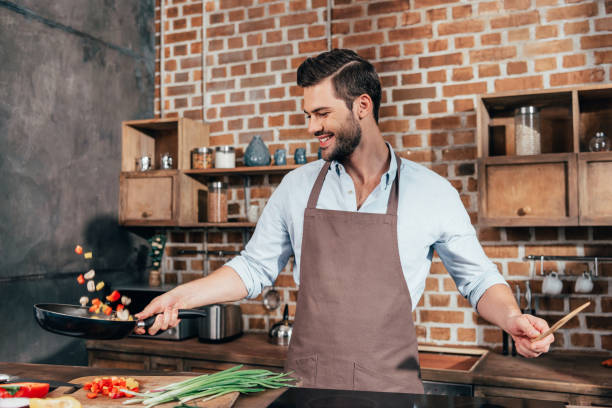 istock joyful young man with apron frying vegetables 841656736