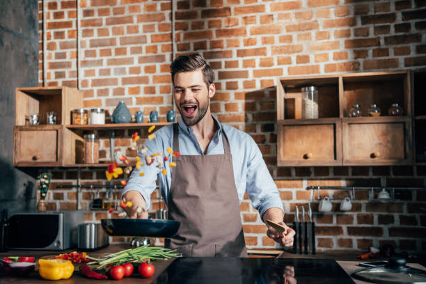 istock stylish young man with apron frying vegetables 841664032