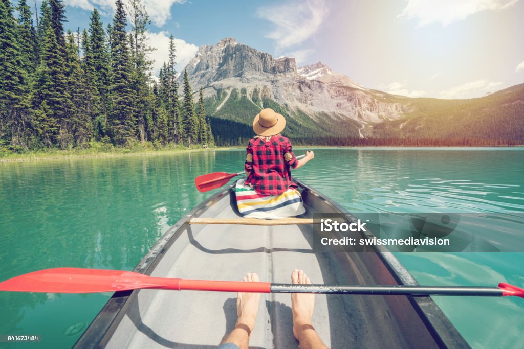 Pov of couple paddling red canoe on turquoise lake View of a young couple canoeing on beautiful mountain lake in Canada Canada Stock Photo